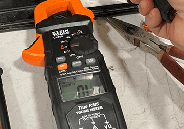 A black and orange digital multimeter with some tools in front of it