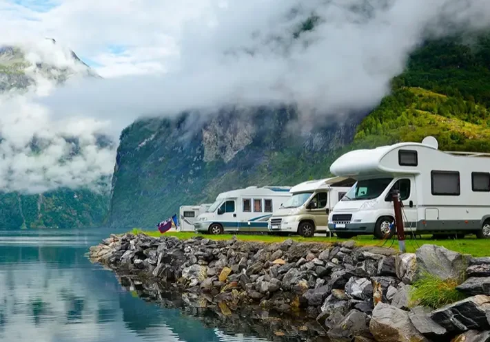 A group of recreational vehicles parked on the side of a lake.