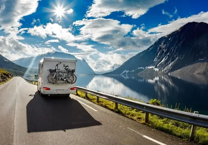 A white rv driving down the road with mountains in the background.